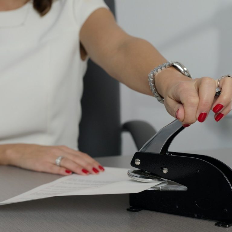 A person using a black notary seal on a stack of paper on a desk.