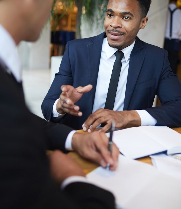 Two men in business attire discussing over papers at a table.